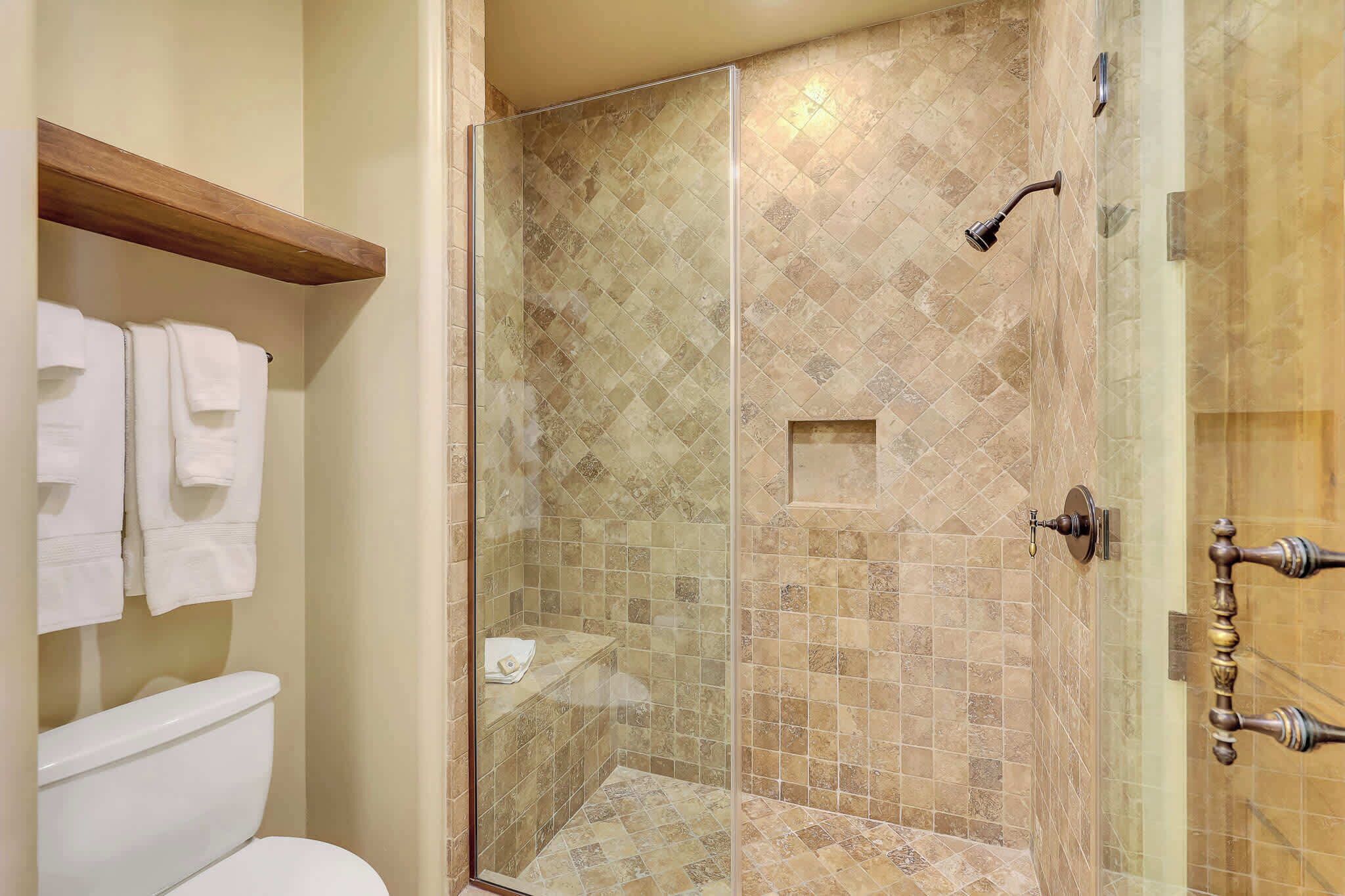 A bathroom with a glass-enclosed shower, a toilet, and a towel rack with towels.