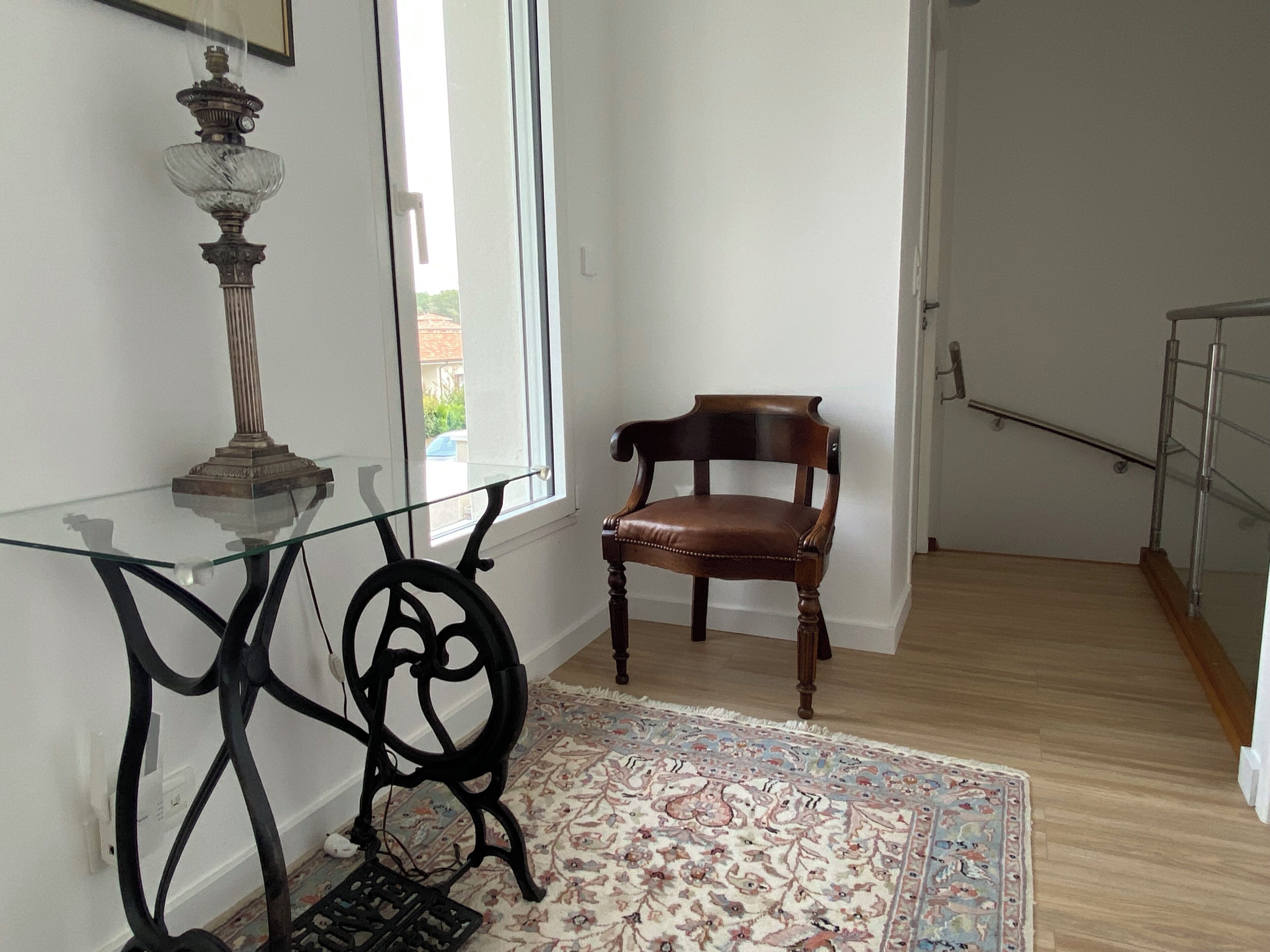 Ein Zimmer mit einem Glastisch, einem Holzstuhl, einem Teppich mit Muster und einer Treppe.