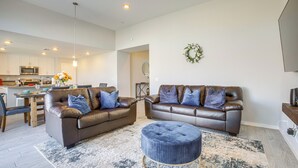 Una sala de estar moderna con dos sofás de cuero marrón, un otoman redondo y una zona de comedor con mesa y sillas de madera.