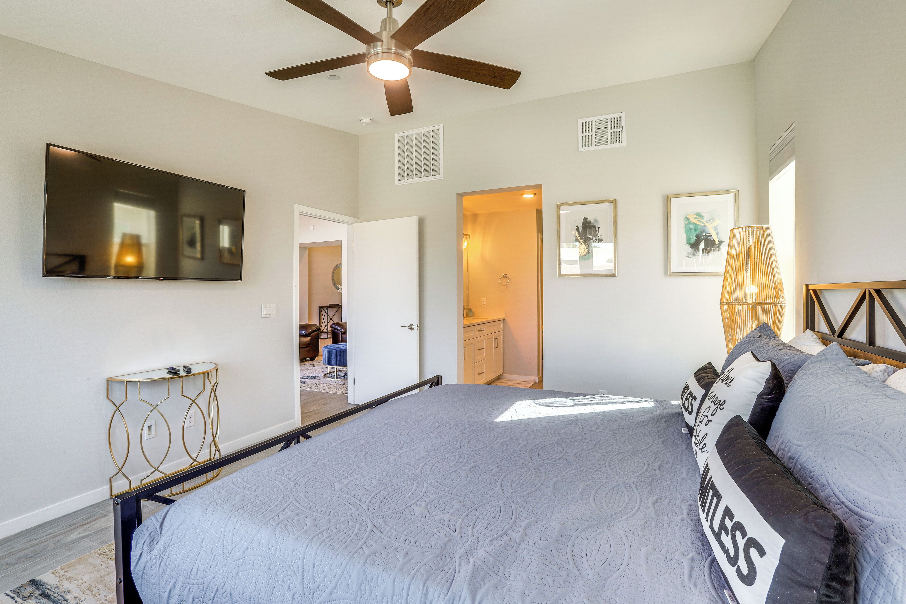 A bedroom with a bed, a ceiling fan, a TV, and a door leading to another room.