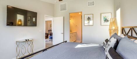 A bedroom with a bed, a ceiling fan, a TV, and a door leading to another room.