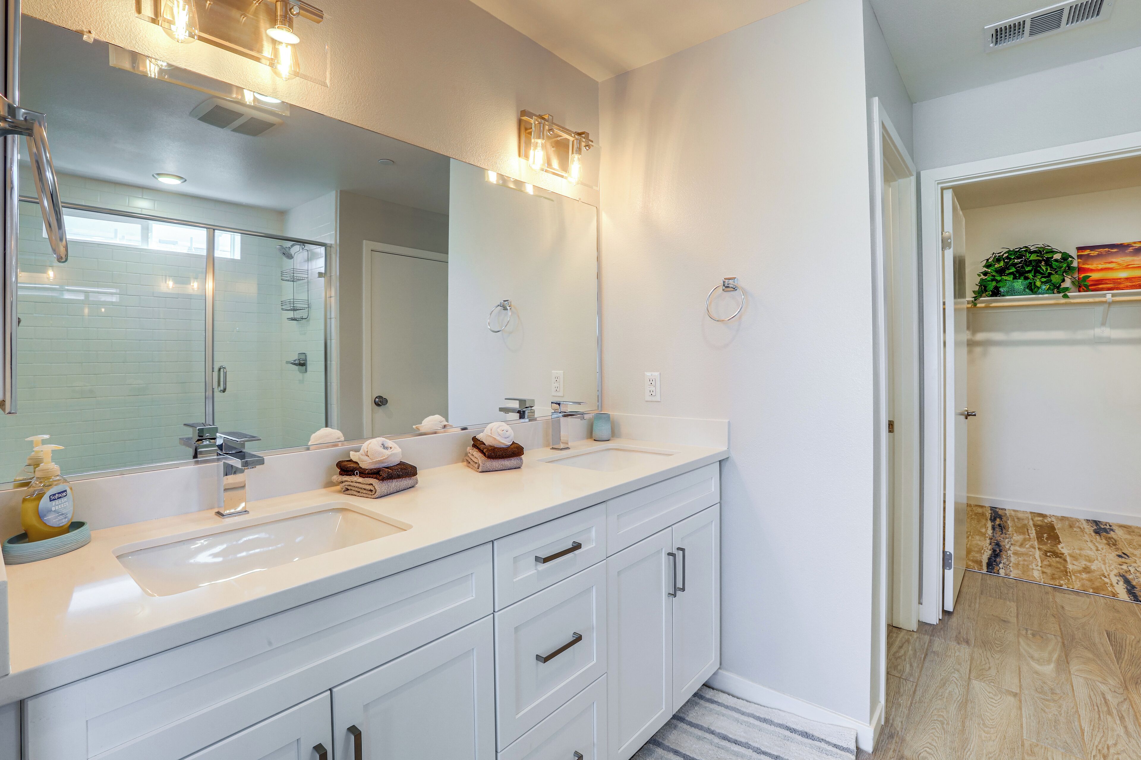 A modern bathroom with a large mirror, two sinks, and a shower.
