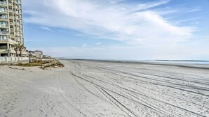 A beach with a building on the left, featuring multiple floors and balconies.