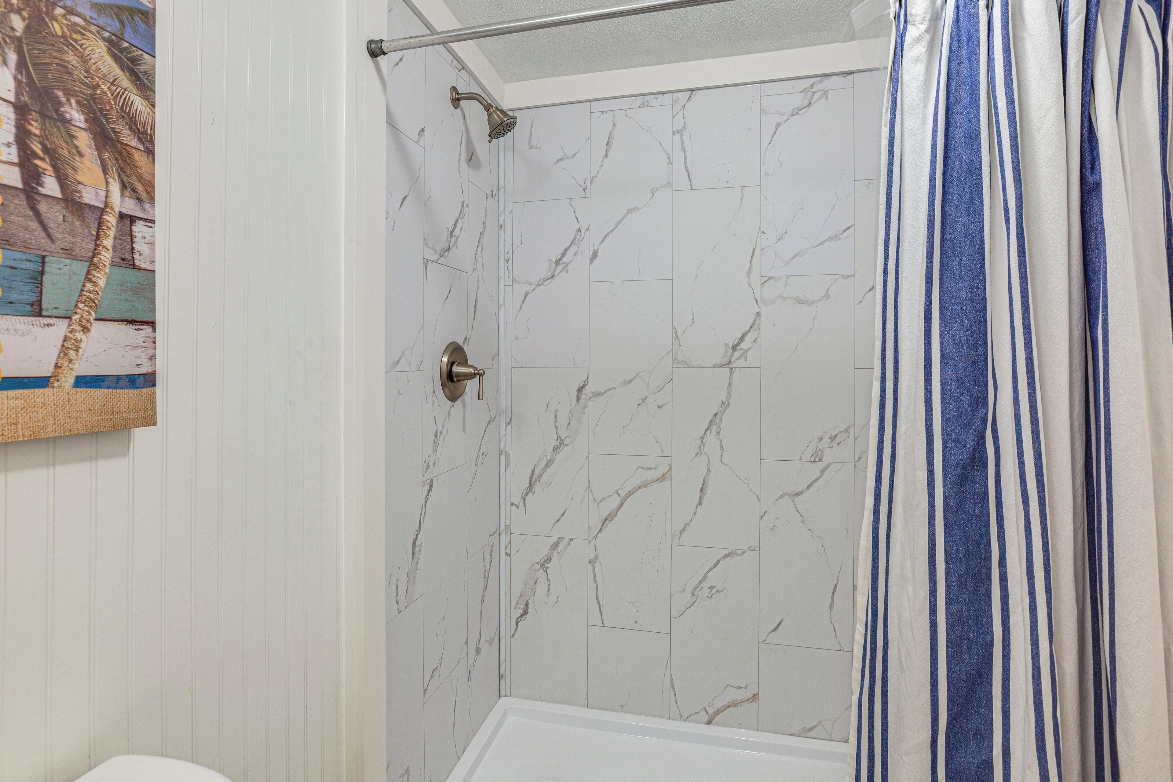 A bathroom with white marble tiles, a shower with a handheld showerhead, and a striped shower curtain.