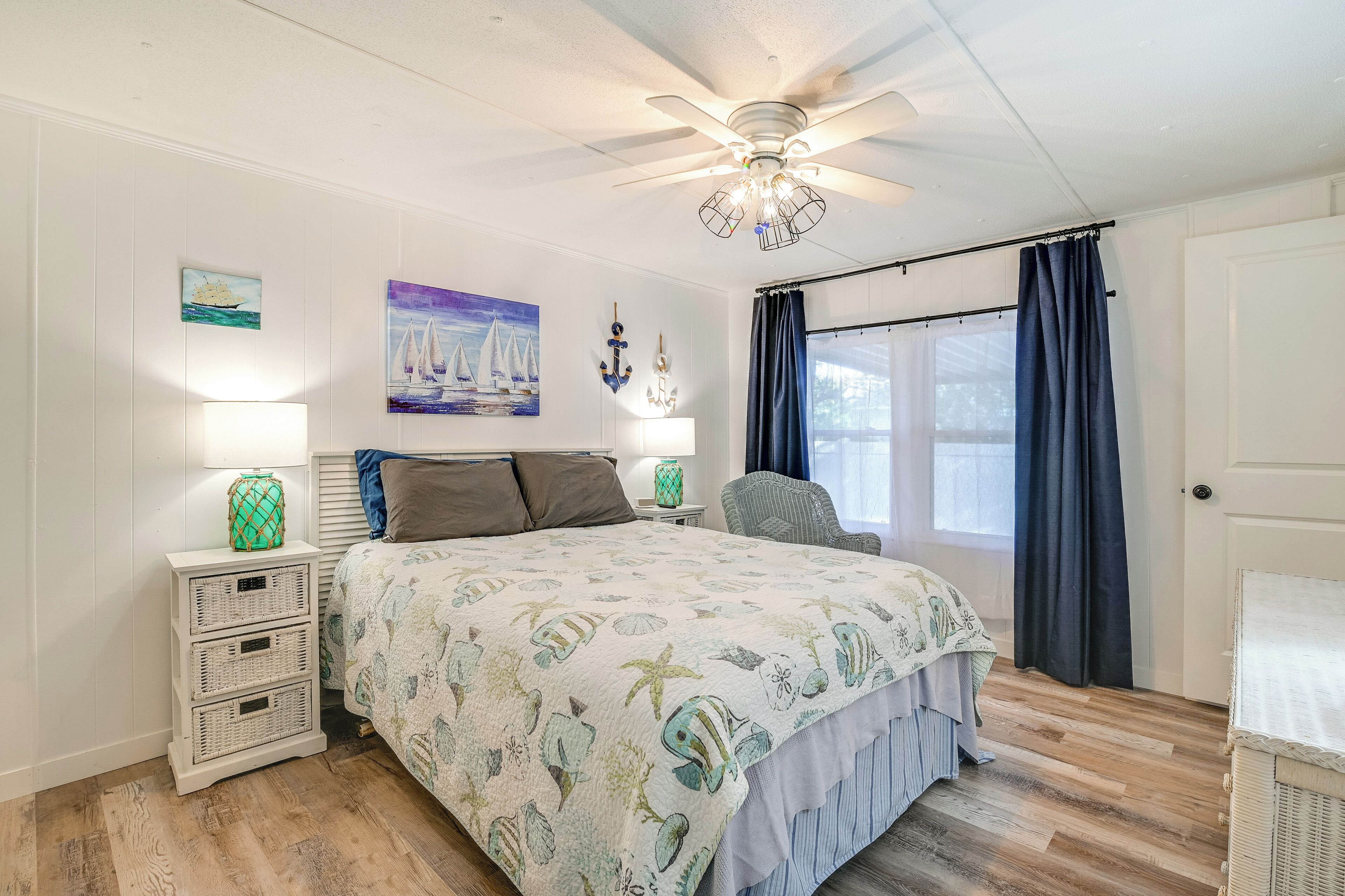 A bedroom with a bed, nightstands, a chair, a ceiling fan, and a window with curtains.