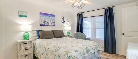 A bedroom with a bed, nightstands, a chair, a ceiling fan, and a window with curtains.
