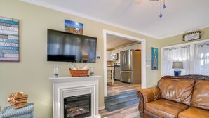 A living room with a fireplace, a television, a sofa, and a kitchen in the background.