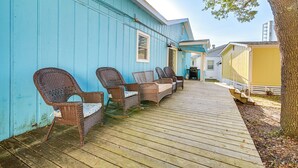 A wooden deck with wicker furniture, a blue building, and a tree.