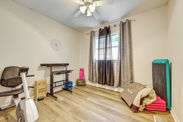 Una habitación con ventilador de techo, equipo de ejercicio, una ventana con cortinas y una puerta.