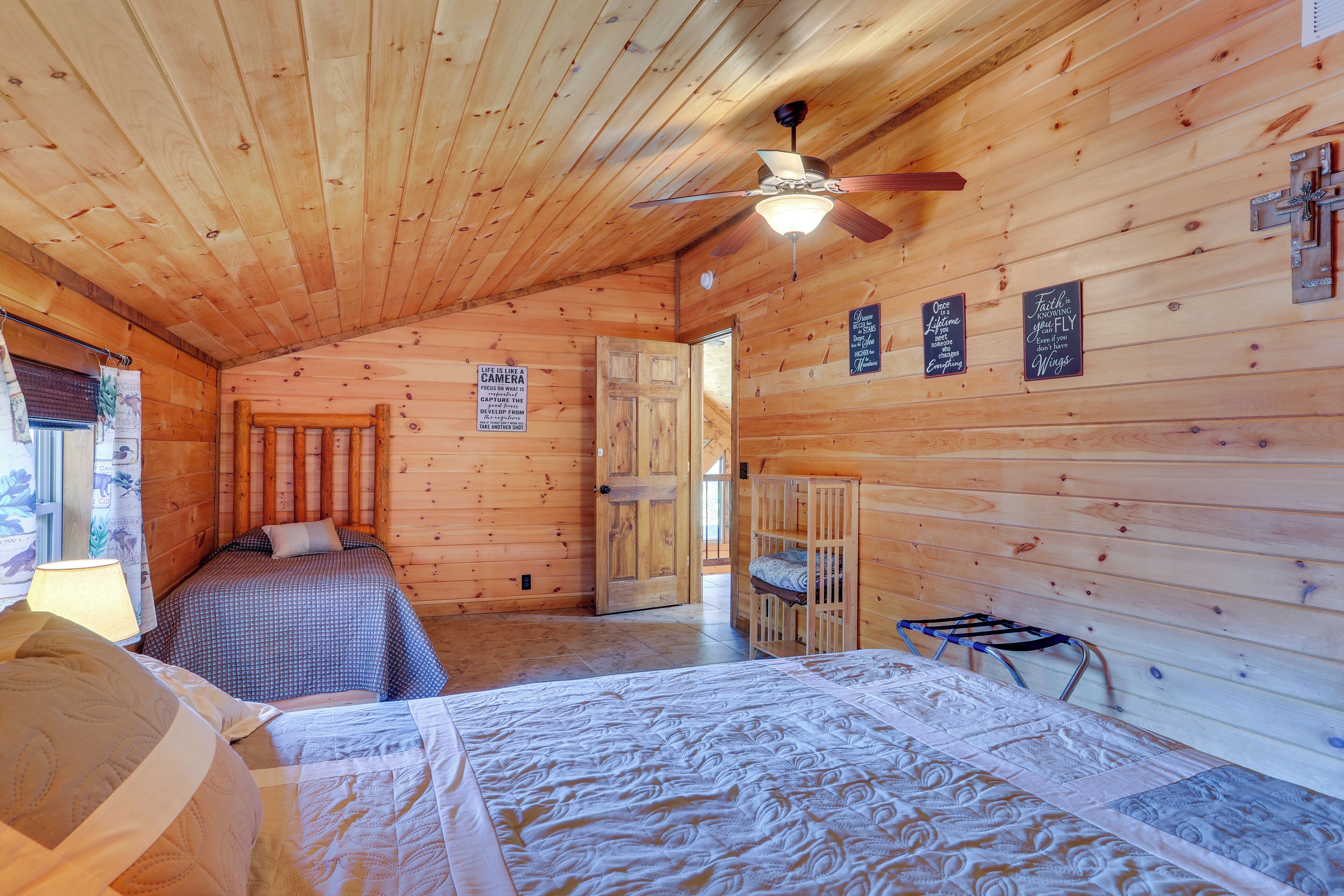Une cabane chaleureuse avec un intérieur en bois, un ventilateur de plafond, un lit avec une courtepointe, un berceau et un panneau accroché au mur.