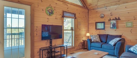 Interior acogedor de una cabaña con techo de madera, televisor, sofá azul y una mesa de centro.