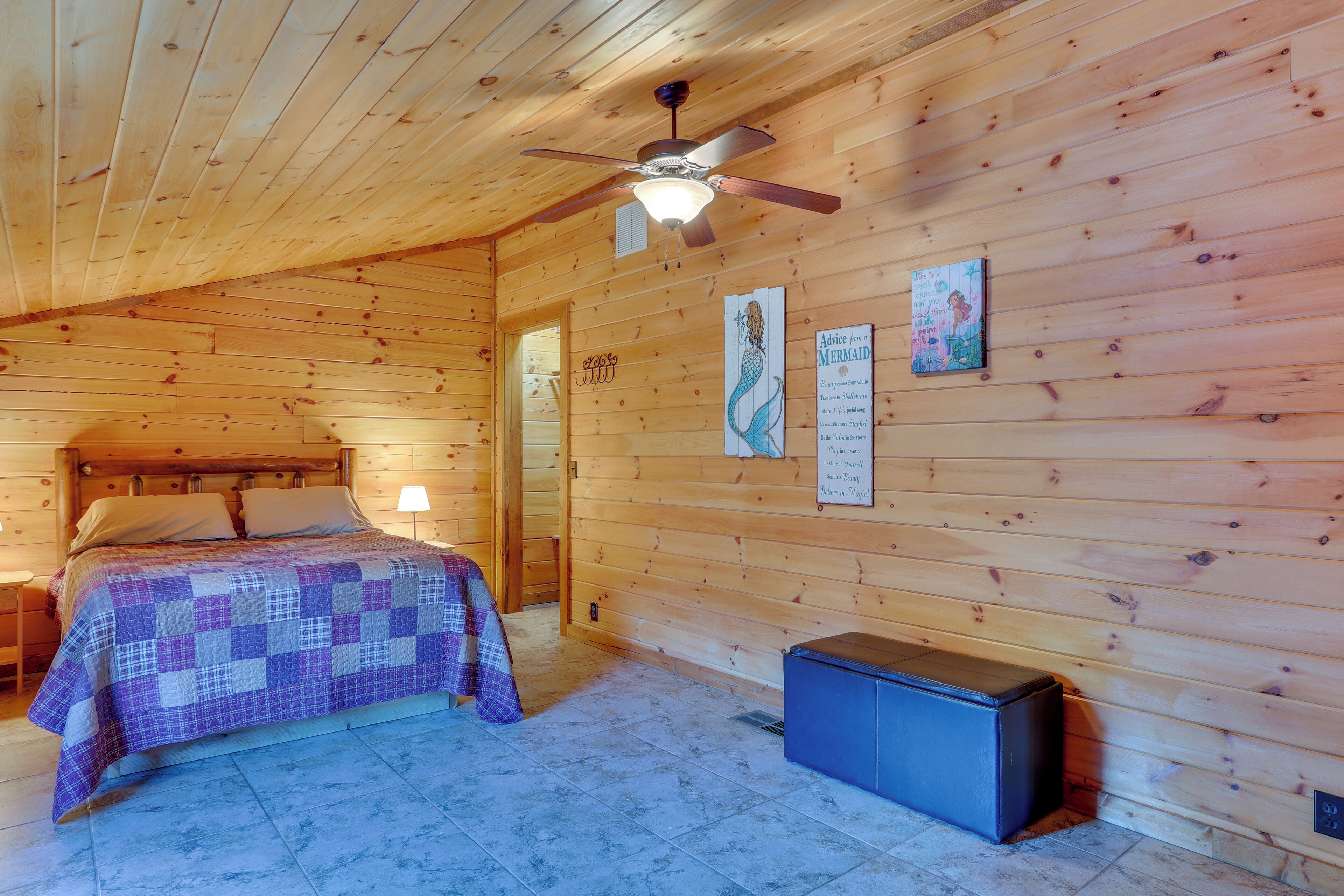 Un dormitorio de cabaña de madera con una cama, un ventilador de techo y un pequeño armario.