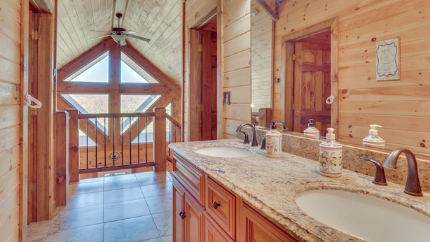 A wooden cabin bathroom with two sinks, a large mirror, and a ceiling fan.