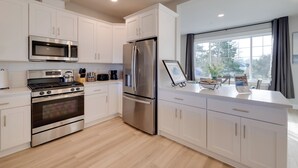 A modern kitchen with stainless steel appliances, white cabinetry, and a large window providing natural light. - Balconies w/ Scenic River Views: Hammond Townhome! (Hammond)