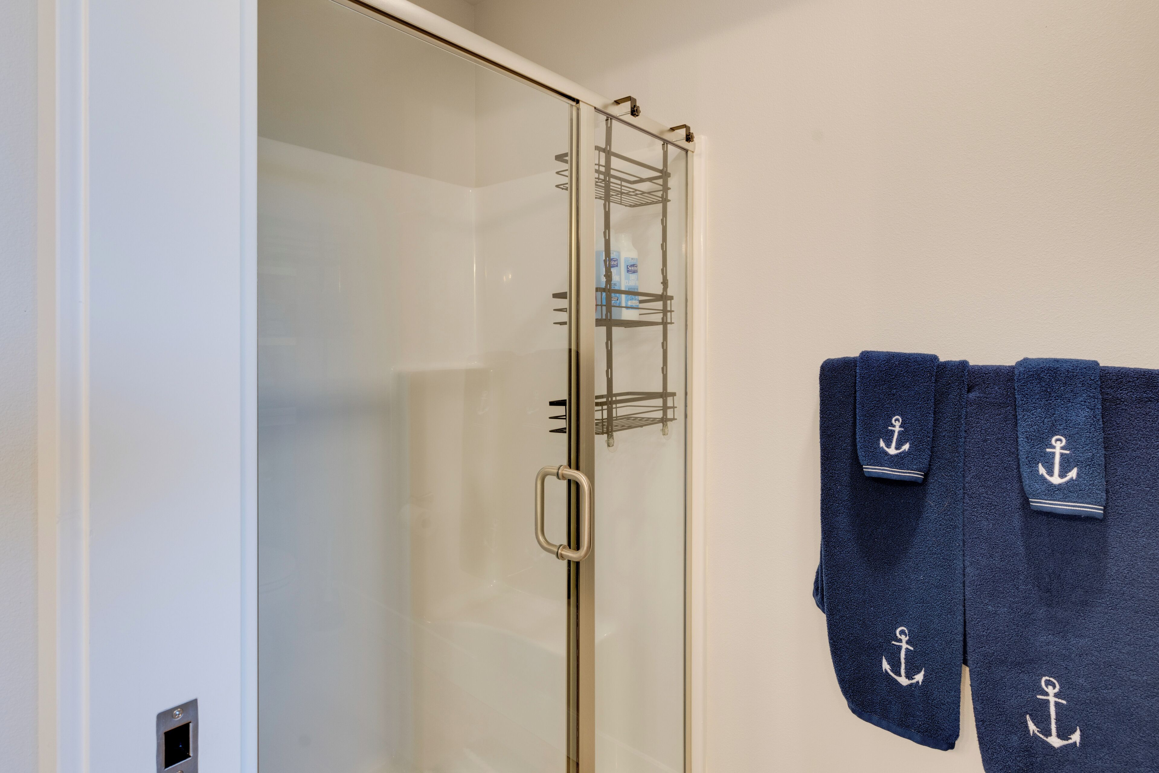 Ein Badezimmer mit Duschkabine aus Glas, einem Handtuchhalter mit dunkelblauen Handtüchern und Ablage für Toilettenartikel.