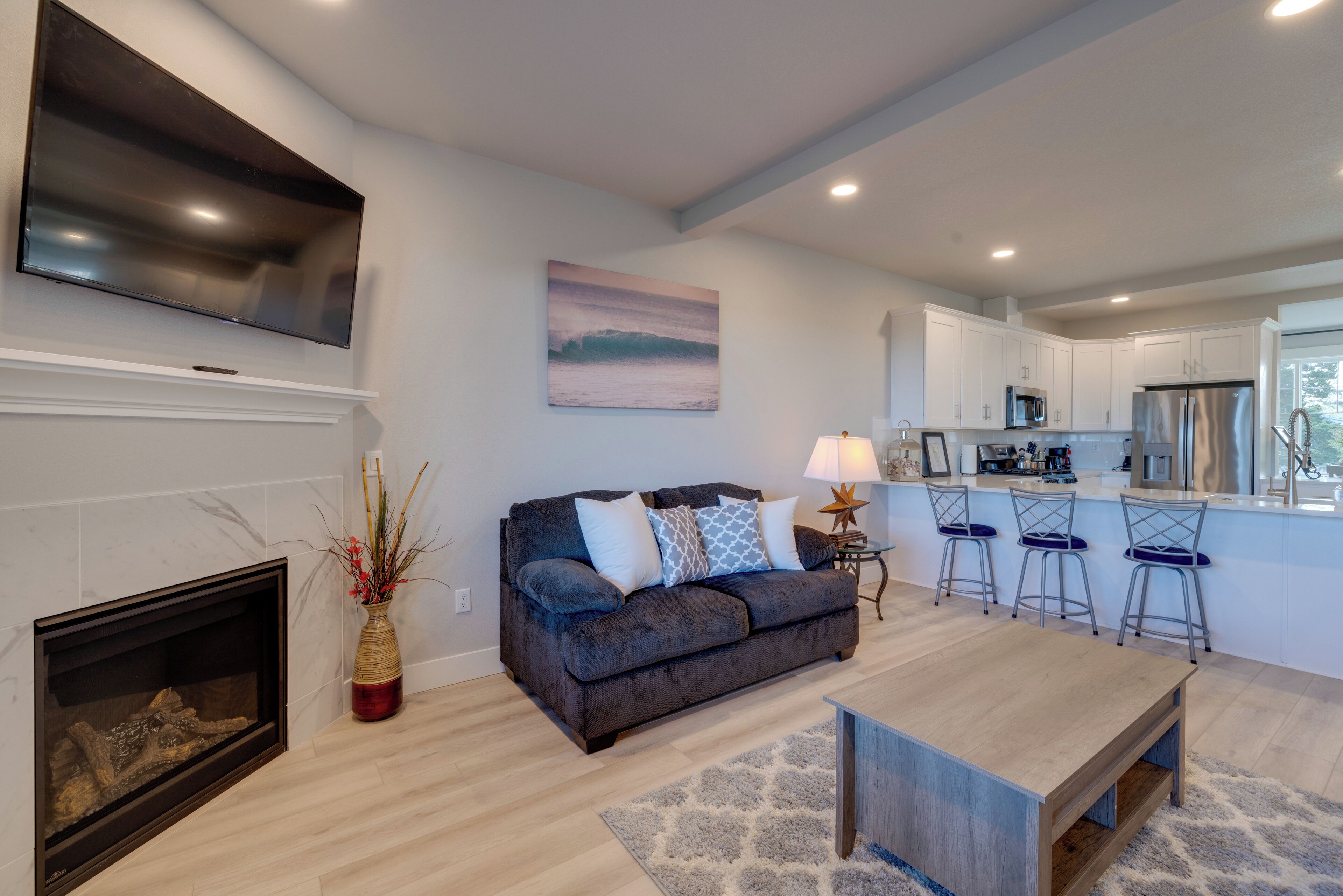 A modern living room with a fireplace, a sofa, a coffee table, and a kitchen area with bar stools.