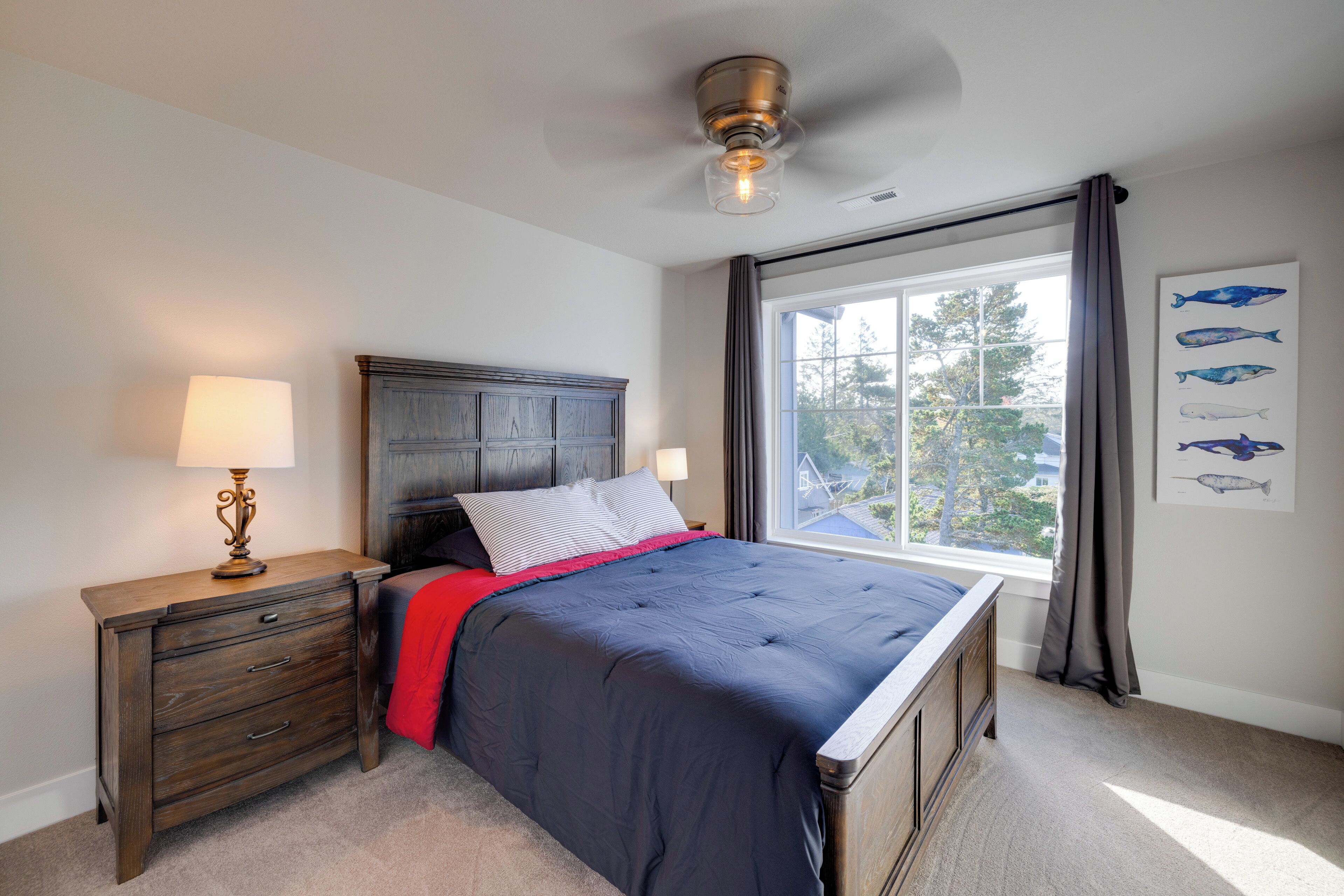 A bedroom with a bed, a nightstand, a lamp, a window with curtains, and a ceiling fan.