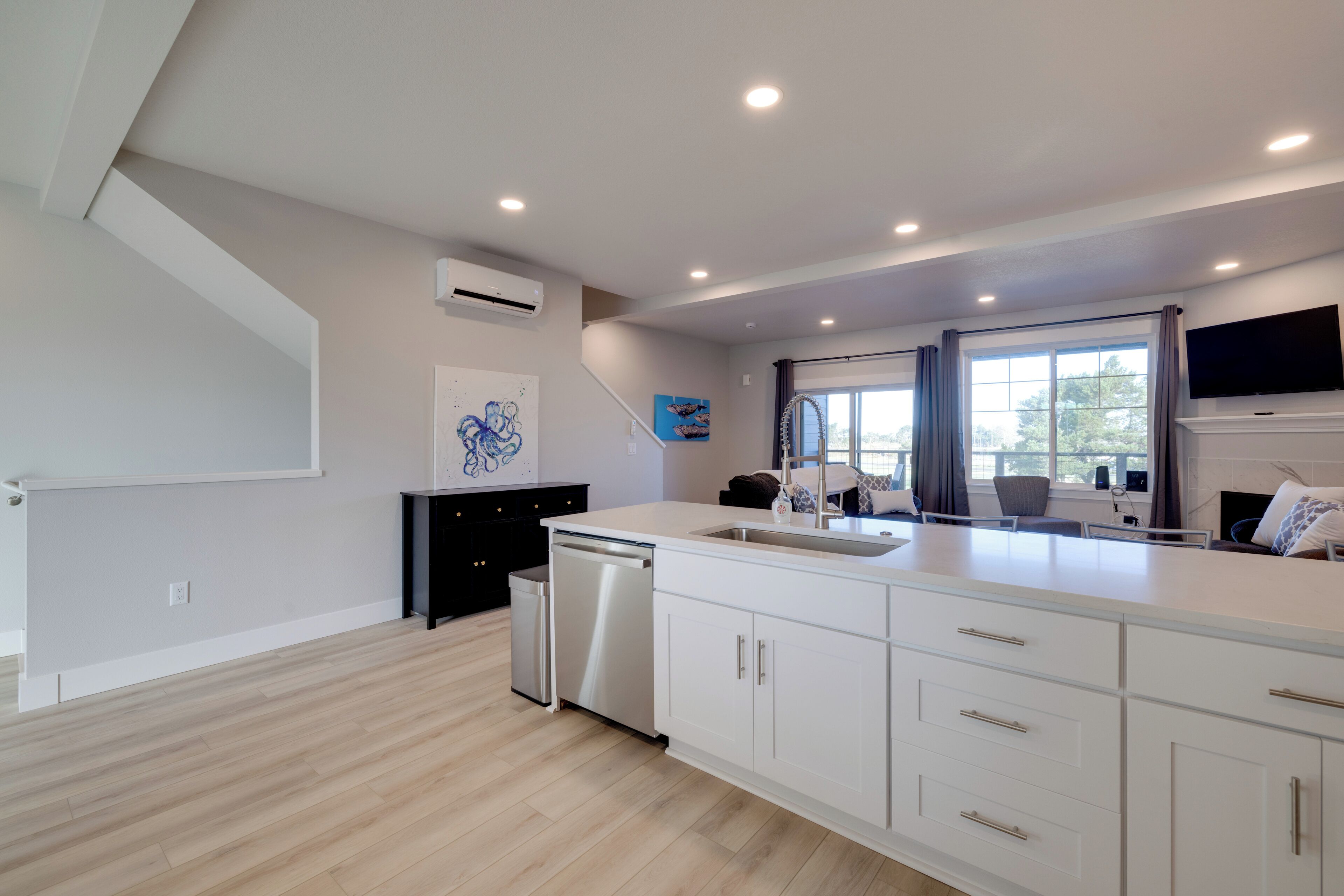 A modern kitchen with white cabinetry, a dishwasher, and a large window with curtains.