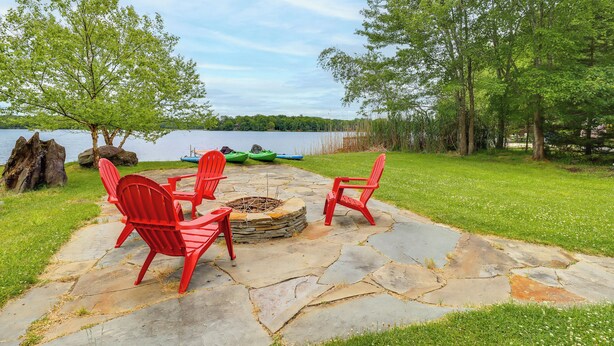A stone patio with red Adirondack chairs, a fire pit, and a view of a lake. - Beach Access, Private Dock: Arrowhead Lake Cabin (Pocono Lake)