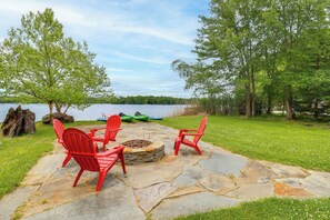 A stone patio with red Adirondack chairs, a fire pit, and a view of a lake. - Beach Access, Private Dock: Arrowhead Lake Cabin (Pocono Lake)