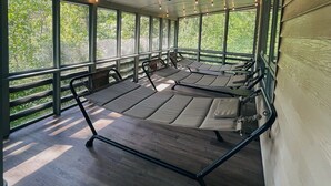 A covered outdoor seating area with multiple tables and chairs, large windows, and string lights. - Hammock House at Bella Vista (Bella Vista)