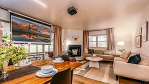 A cozy living room with a fireplace, a dining area with a wooden table, and a large TV screen displaying a scenic landscape. - Hammock House at Bella Vista (Bella Vista)