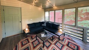 A modern living room with a sectional sofa, a coffee table, and a patterned rug. There are large windows providing natural light and a view of the outside. - Hammock House at Bella Vista (Bella Vista)