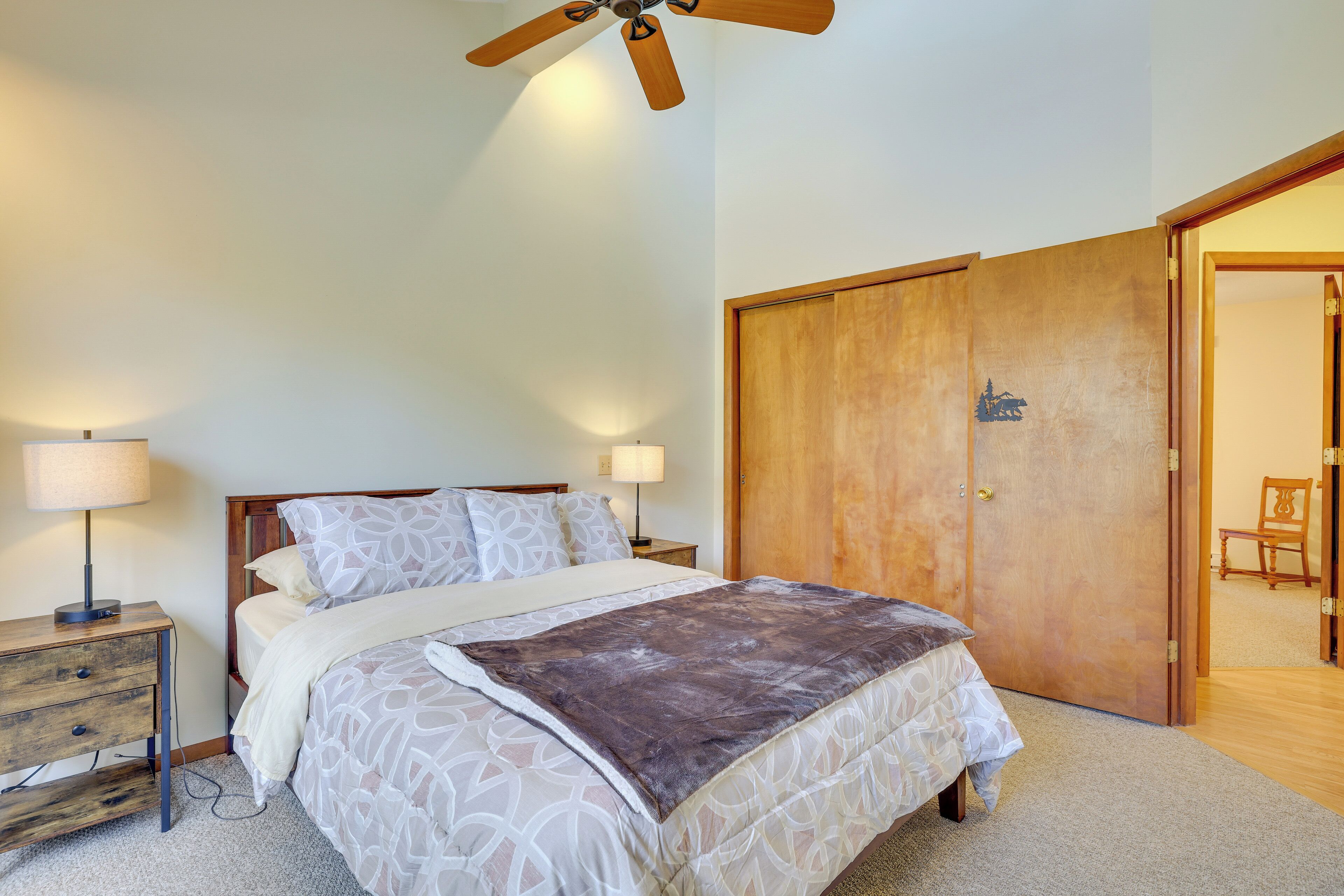 Un dormitorio con cama, cabecera de madera, dos mesitas de noche con l ámparas, un armario de madera y un ventilador de techo.