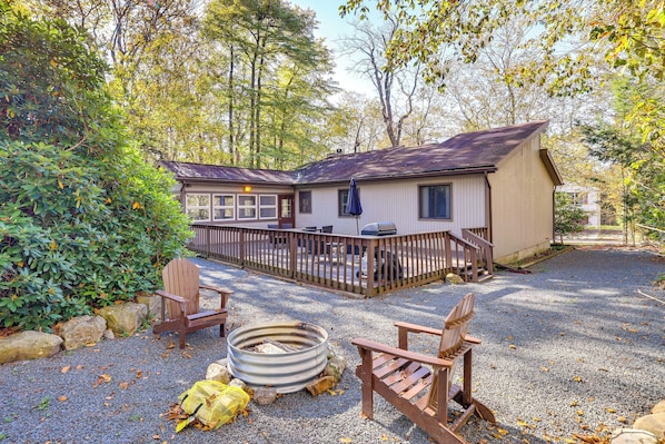 A cabin with a deck, surrounded by trees and gravel.