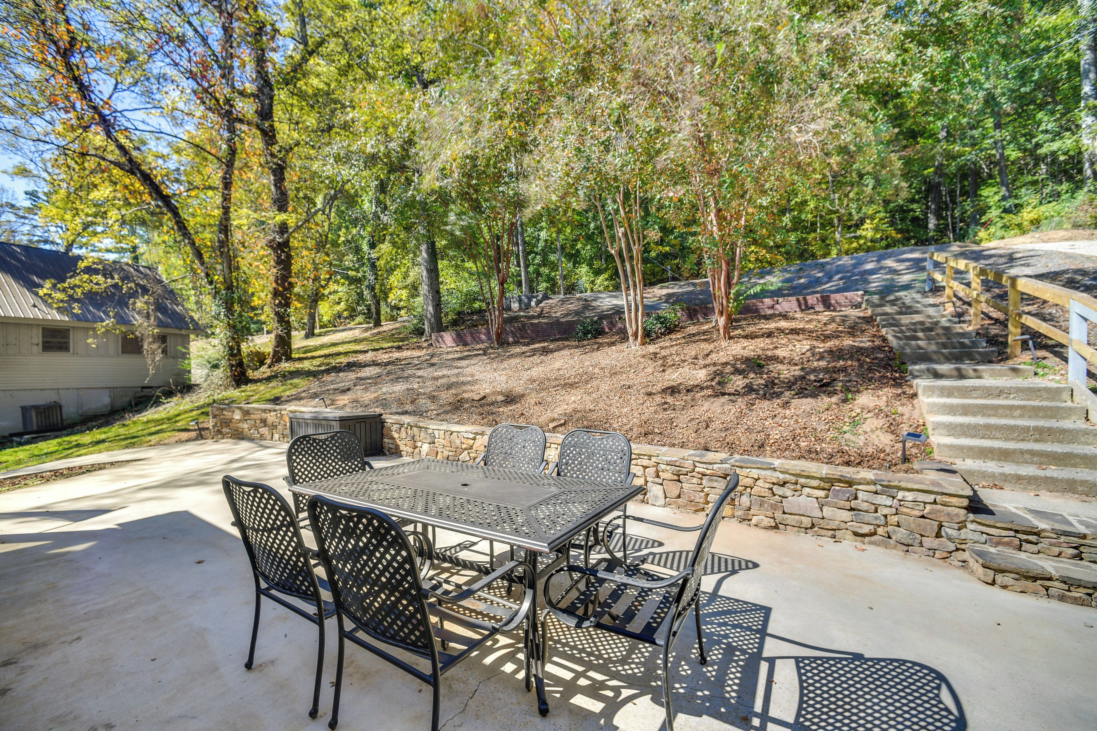 A patio with a metal table and chairs, surrounded by a stone wall and trees.