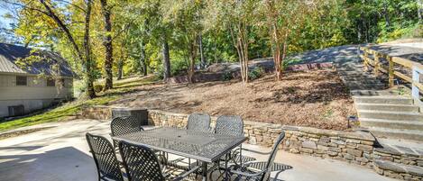 A patio with a metal table and chairs, surrounded by a stone wall and trees.