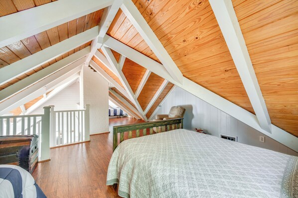 A bedroom with a sloped ceiling, wooden beams, a bed, a chair, and a small table. - Dock + Panoramic Views: Guntersville Lake Retreat! (Scottsboro)