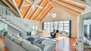 Ein geräumiges Wohnzimmer mit hohen Decken, Holzbalken, einem grauen Ecksofa, einem Essbereich und großen Fenstern mit Blick.