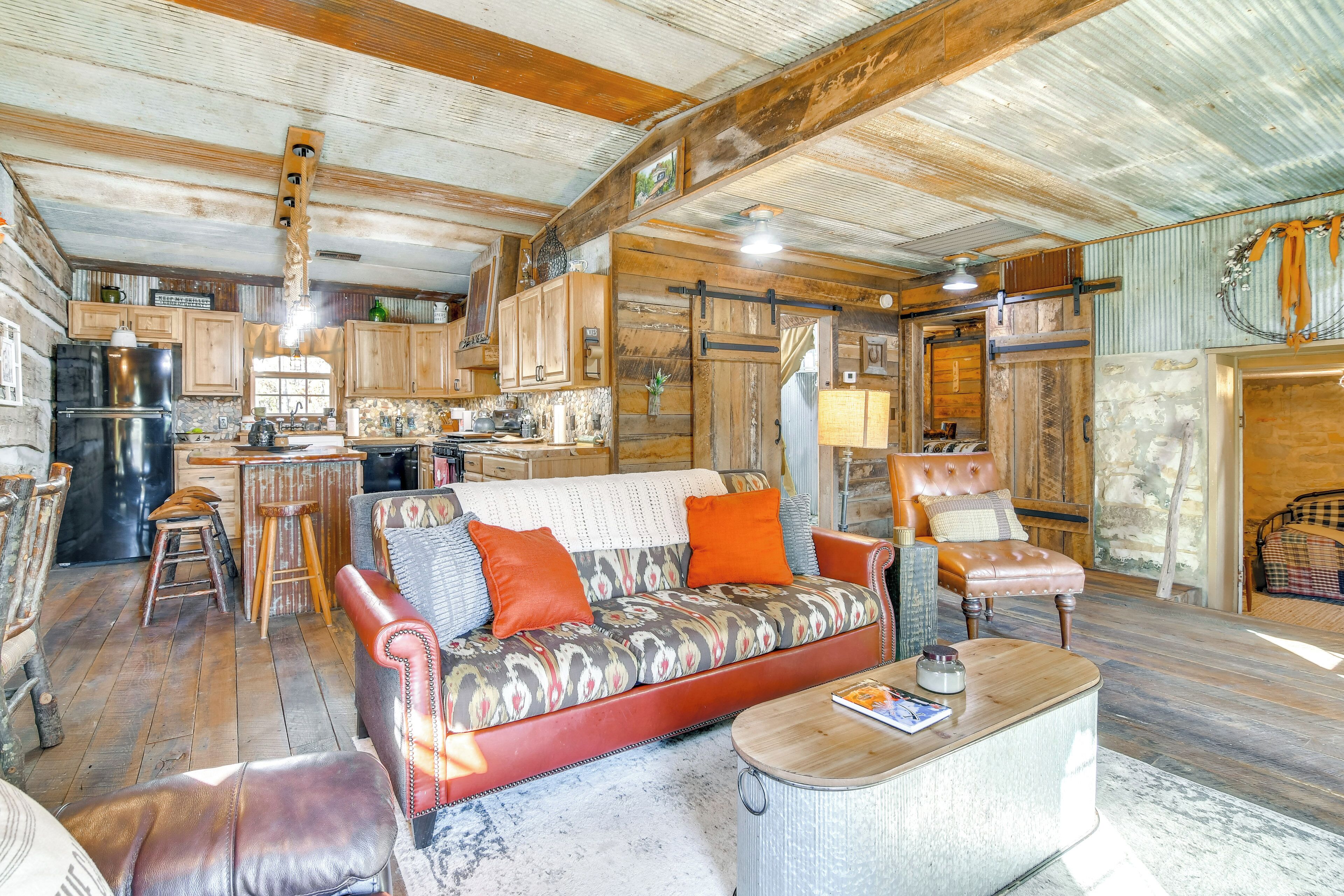 Un interno rustico con soffitto in legno, un divano con rivestimento decorato, una poltrona in pelle e un angolo bar con sgabelli.