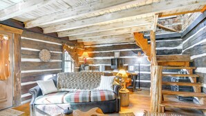 L’intérieur d’une cabane en rondins, avec un canapé à carreaux, un escalier en bois et une décoration rustique.