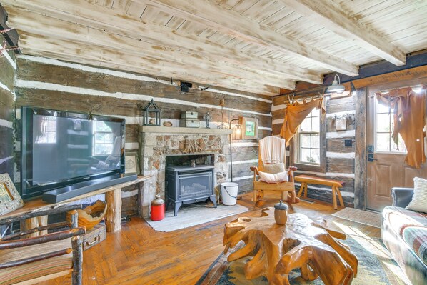 A rustic cabin interior with a large TV, stone fireplace, wooden furniture, and a cozy seating area. - 1/2-mi to Lake: Cabin on 43 Acres in Shell Knob! (Shell Knob)