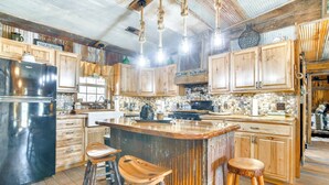 Une cuisine rustique avec des meubles en bois, un grand îlot central doté de tabourets et un réfrigérateur noir.