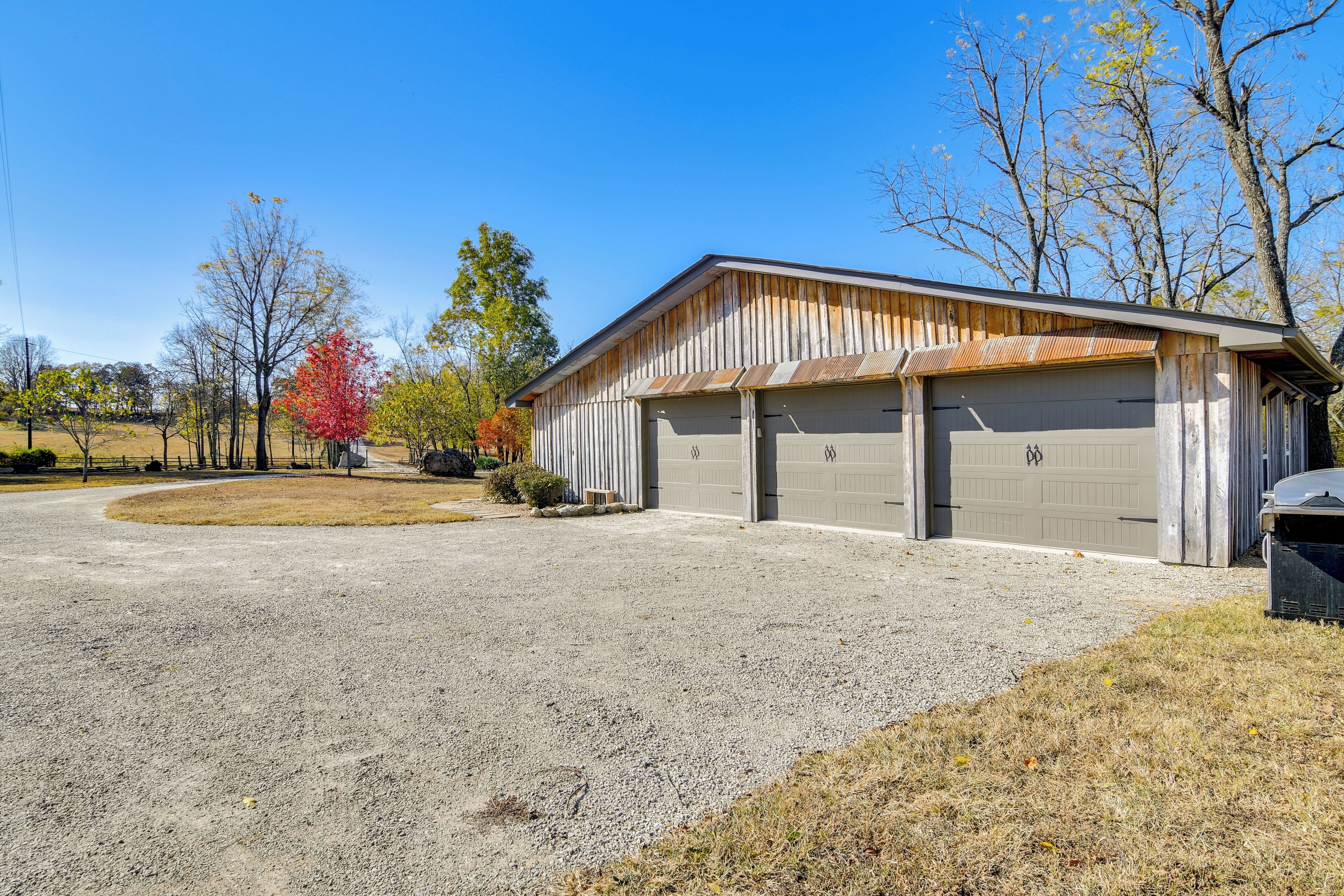 Un bâtiment d’un seul étage avec un garage, entouré d’une allée en gravier et d’une végétation clairsemée.