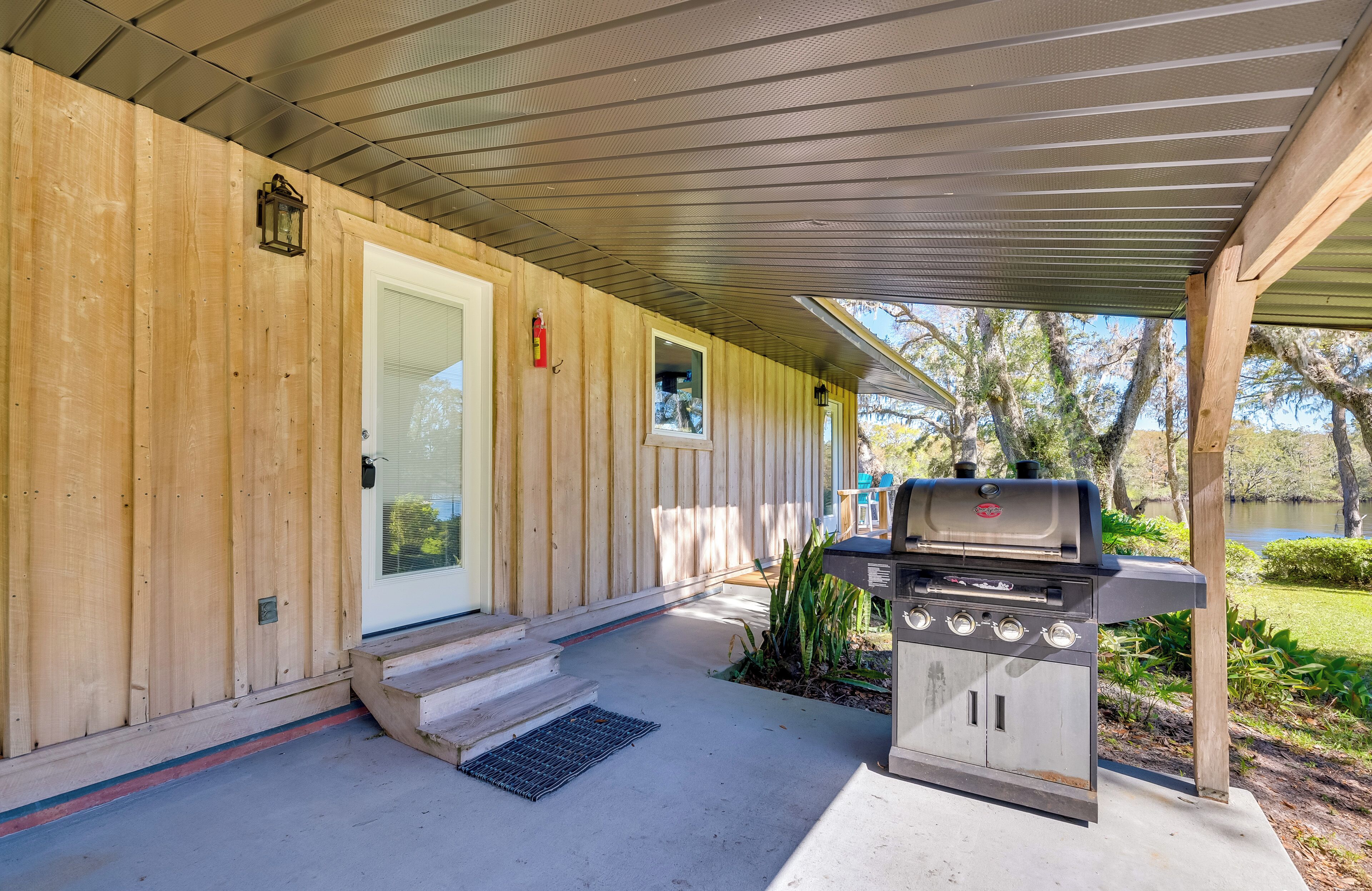 A covered porch with a grill, wooden siding, and a door.