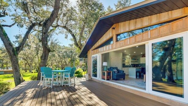 A wooden deck with outdoor seating, large windows, and a view of trees. - Waterfront Home w/ Boat Dock & Slip in Old Town! (Old Town)