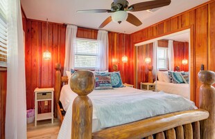 Quarto com painéis de madeira, cama, mesas de cabeceira, ventilador de teto e um espelho grande.