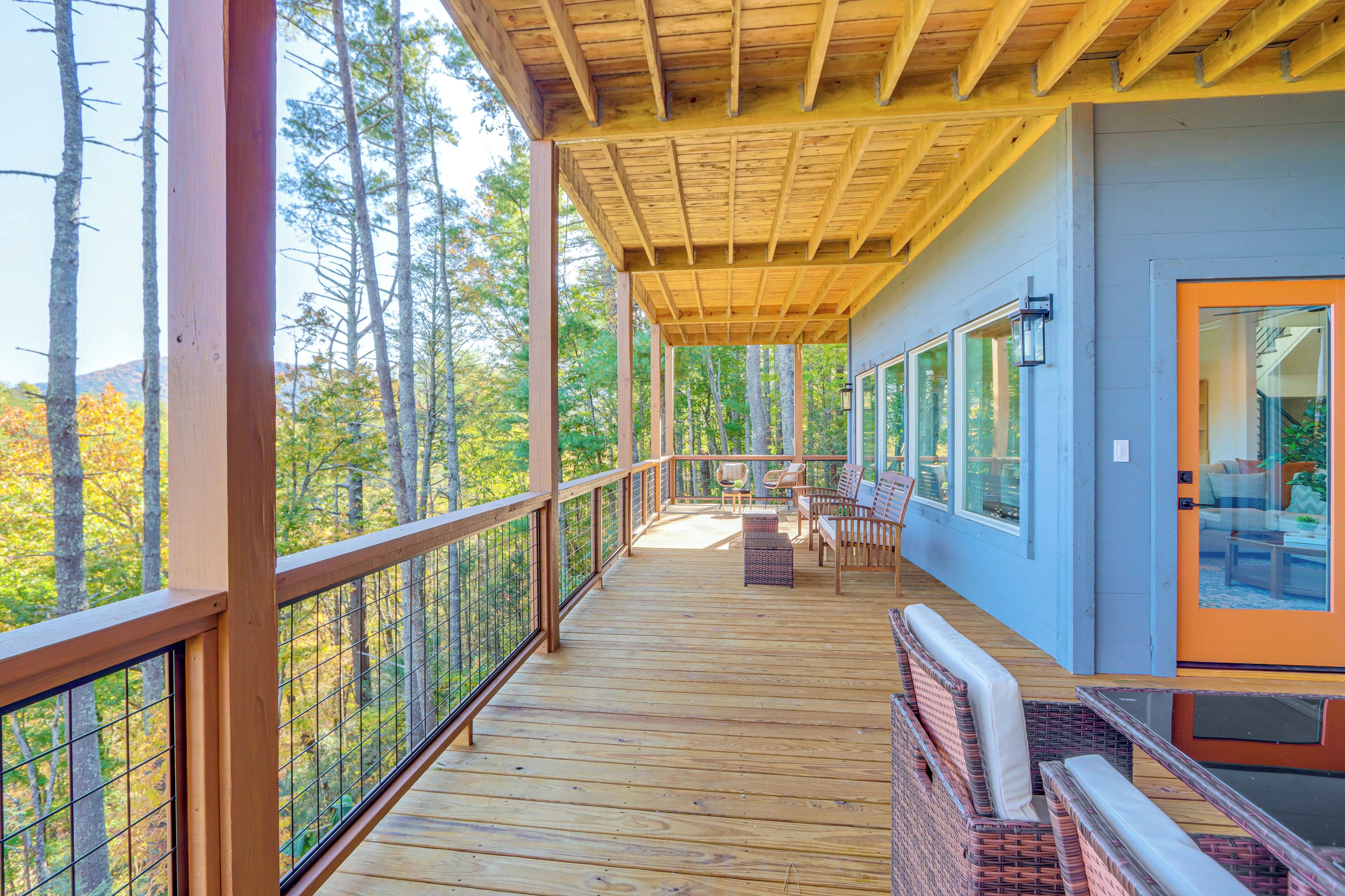 Une terrasse en bois avec une rambarde, des sièges d’extérieur et une vue sur les arbres.