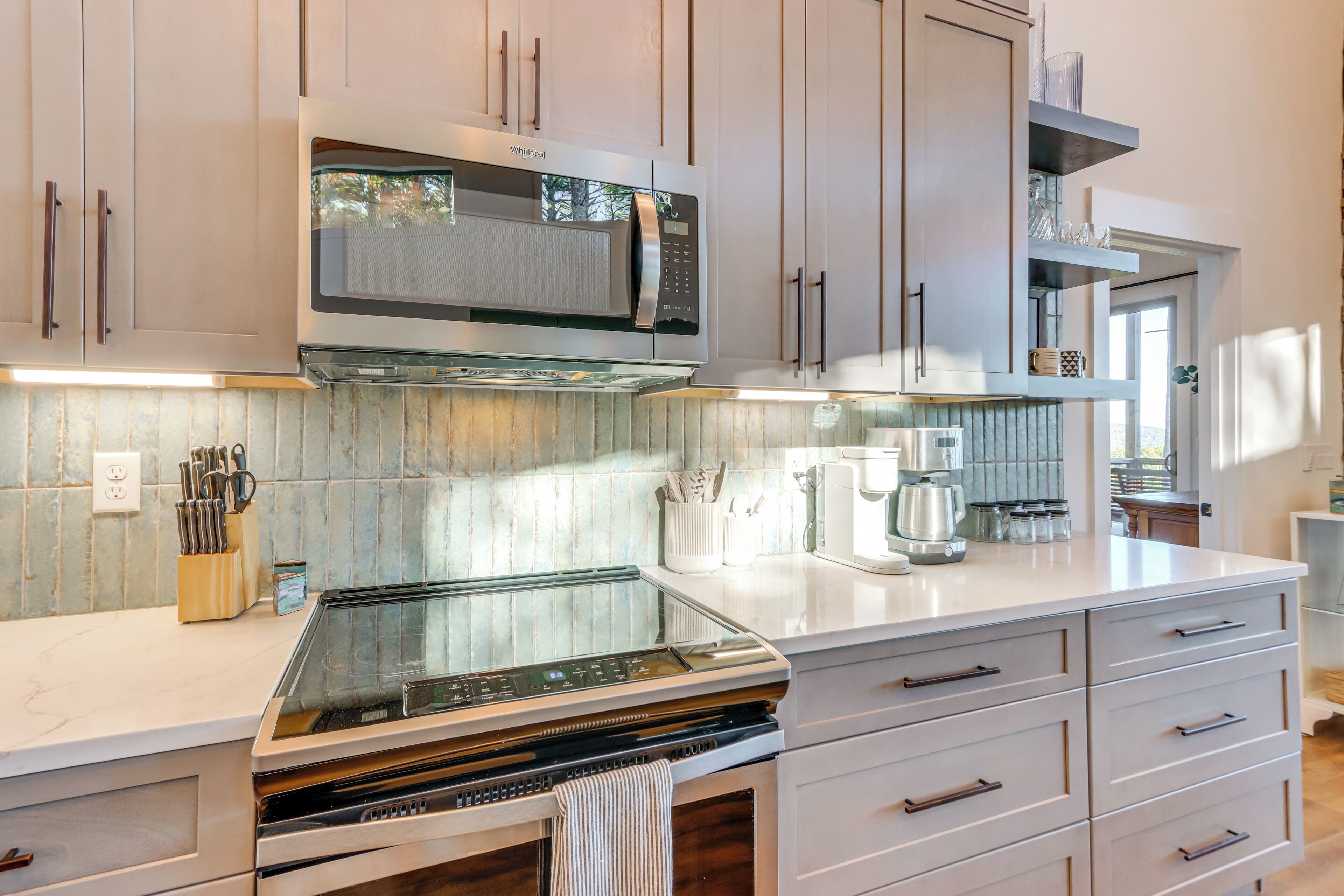 Una cocina moderna con microondas integrado, horno y electrodomésticos de acero inoxidable. Se observan armarios de madera y una encimera blanca.