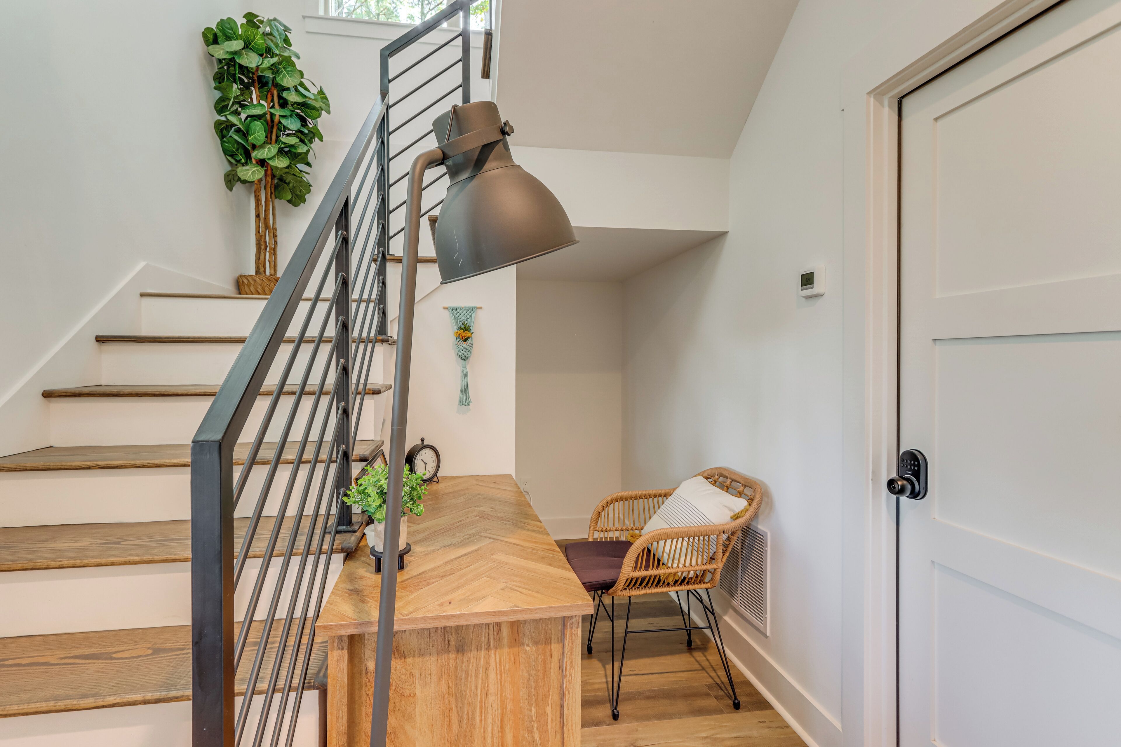 Un escalier avec des finitions en bois, une rampe en métal, une table avec une chaise en osier et un luminaire suspendu.
