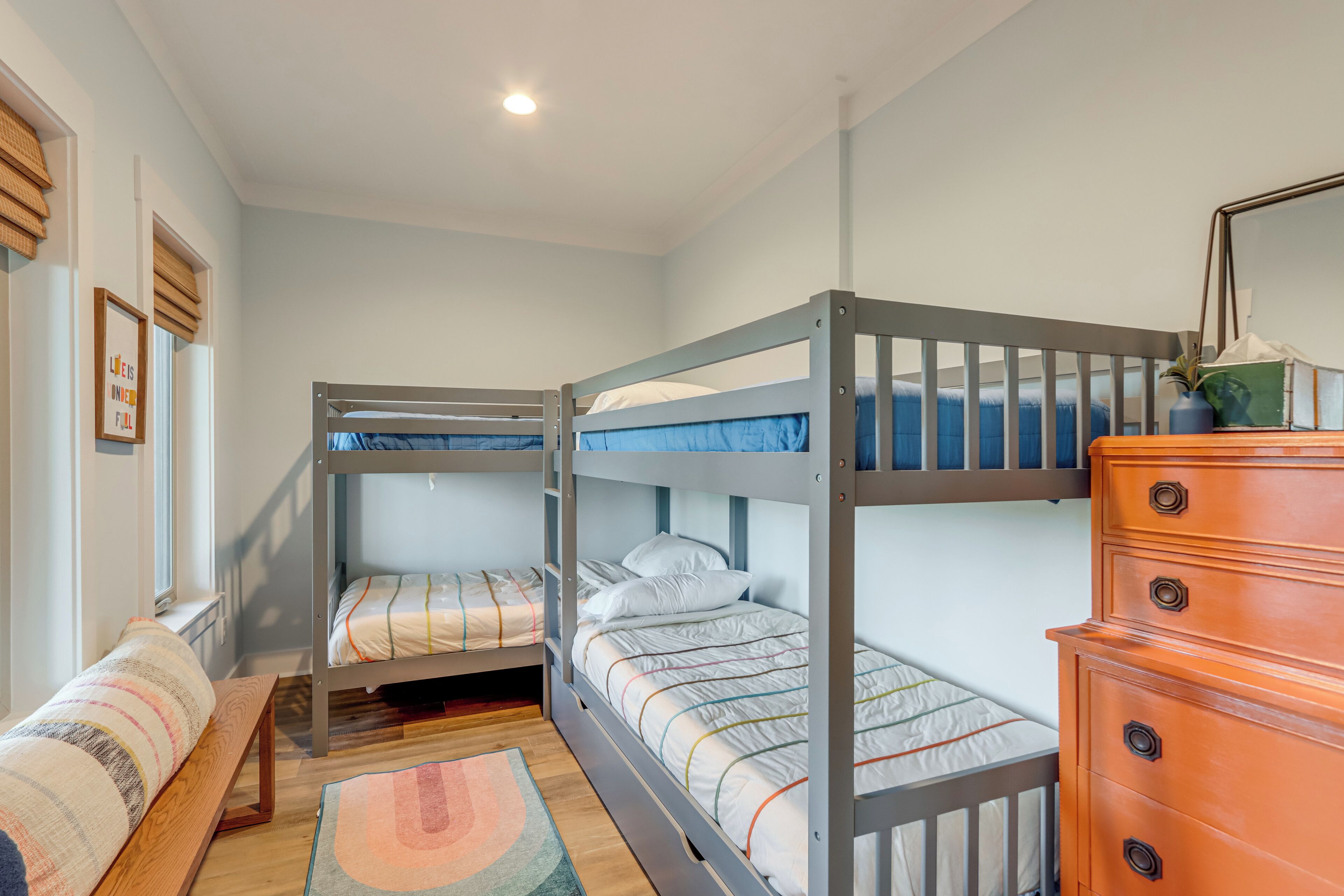 A bunk bed room with a wooden dresser and a bench.