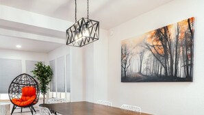 Ein Essbereich mit Holztisch, weißen Stühlen, einer Hängeleuchte und einem Gemälde an der Wand.