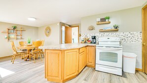 A kitchen with wooden cabinets, a white stove, and a dining area with a table and chairs. - Steps to Long Lake: Cabin w/ Patio in Harrison! (Harrison)
