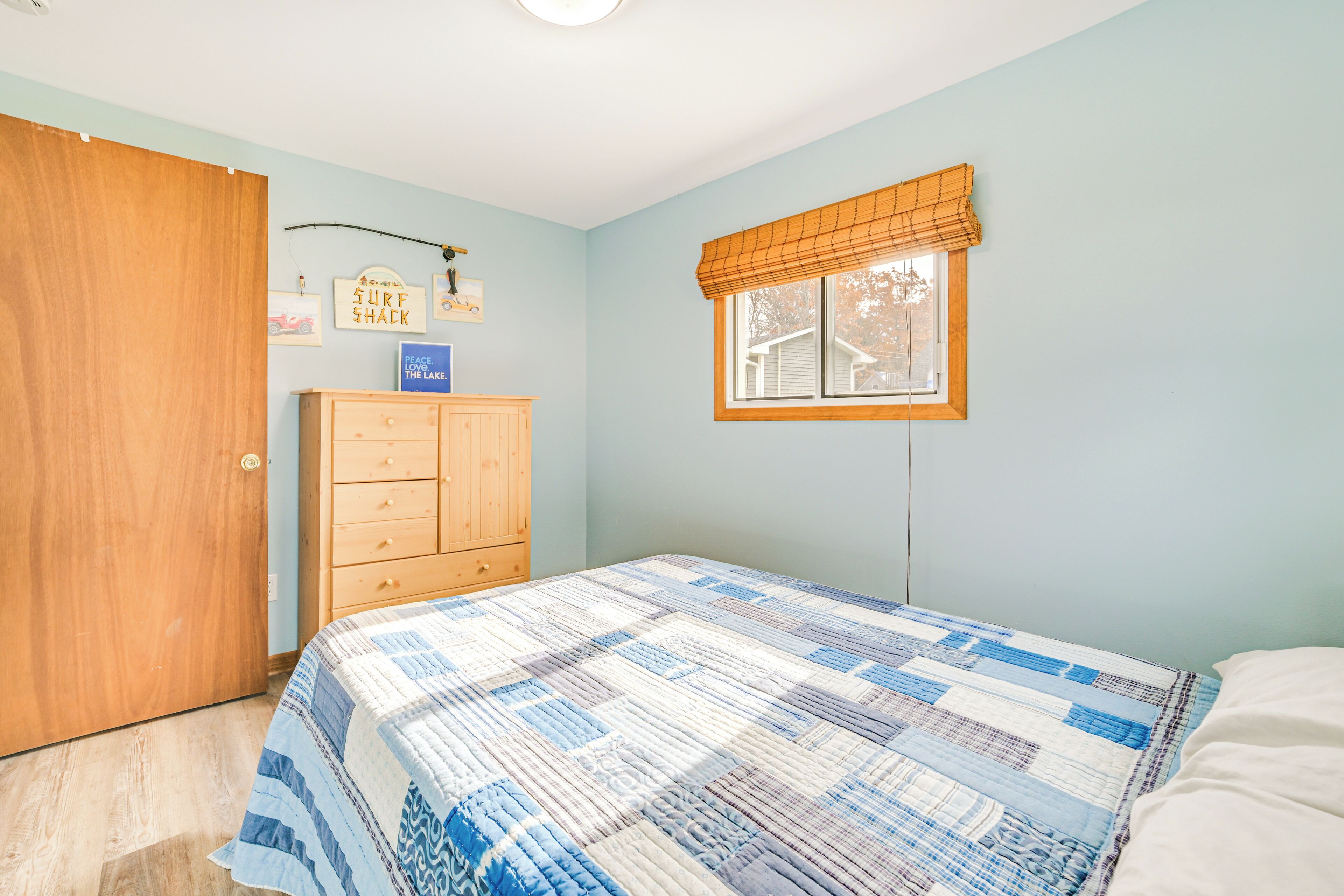 A bedroom with a bed, a wooden dresser, a window with blinds, and wall decorations.