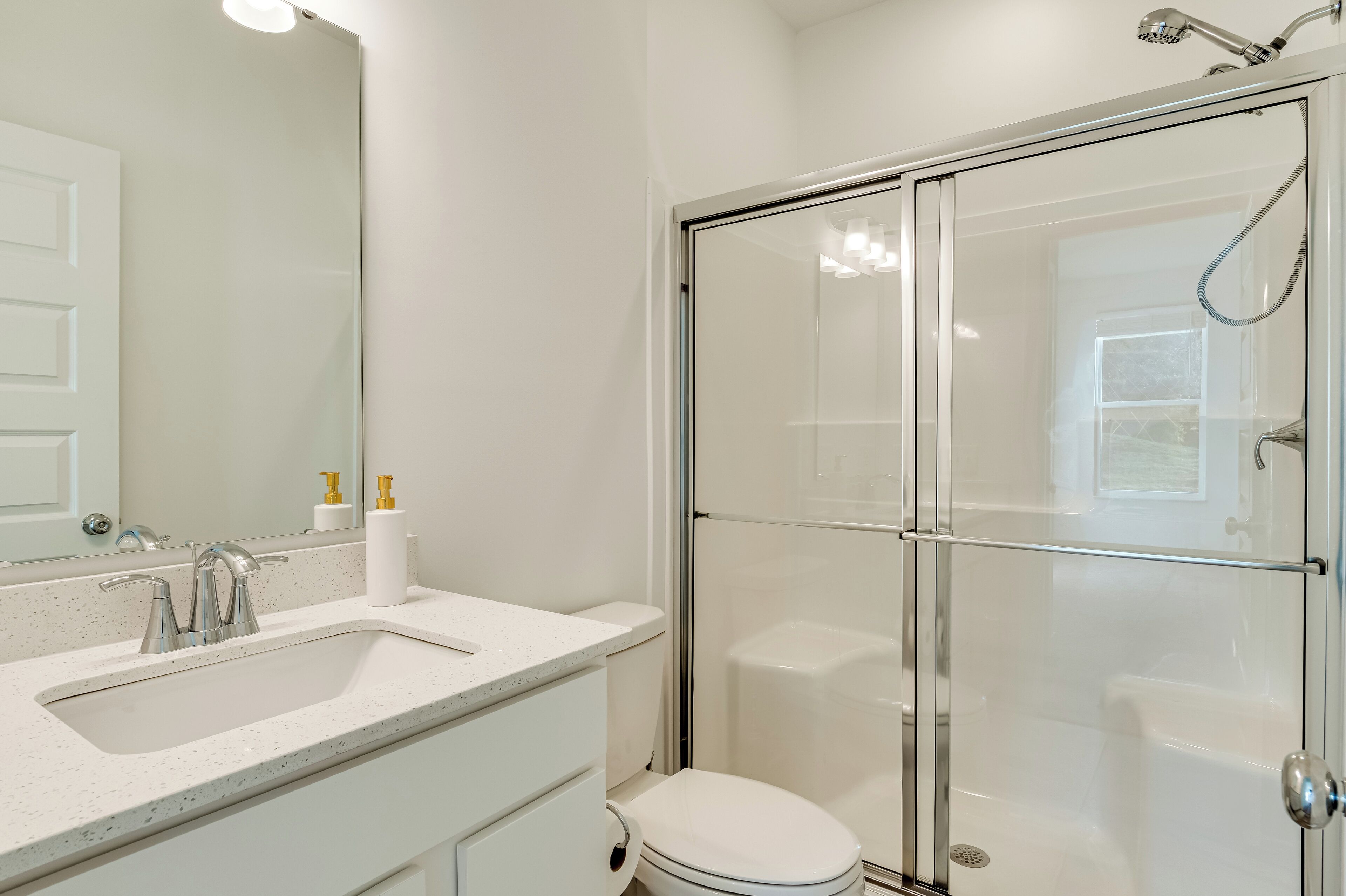 A modern bathroom with a glass-enclosed shower, a white sink with a double-handle faucet, and a toilet.
