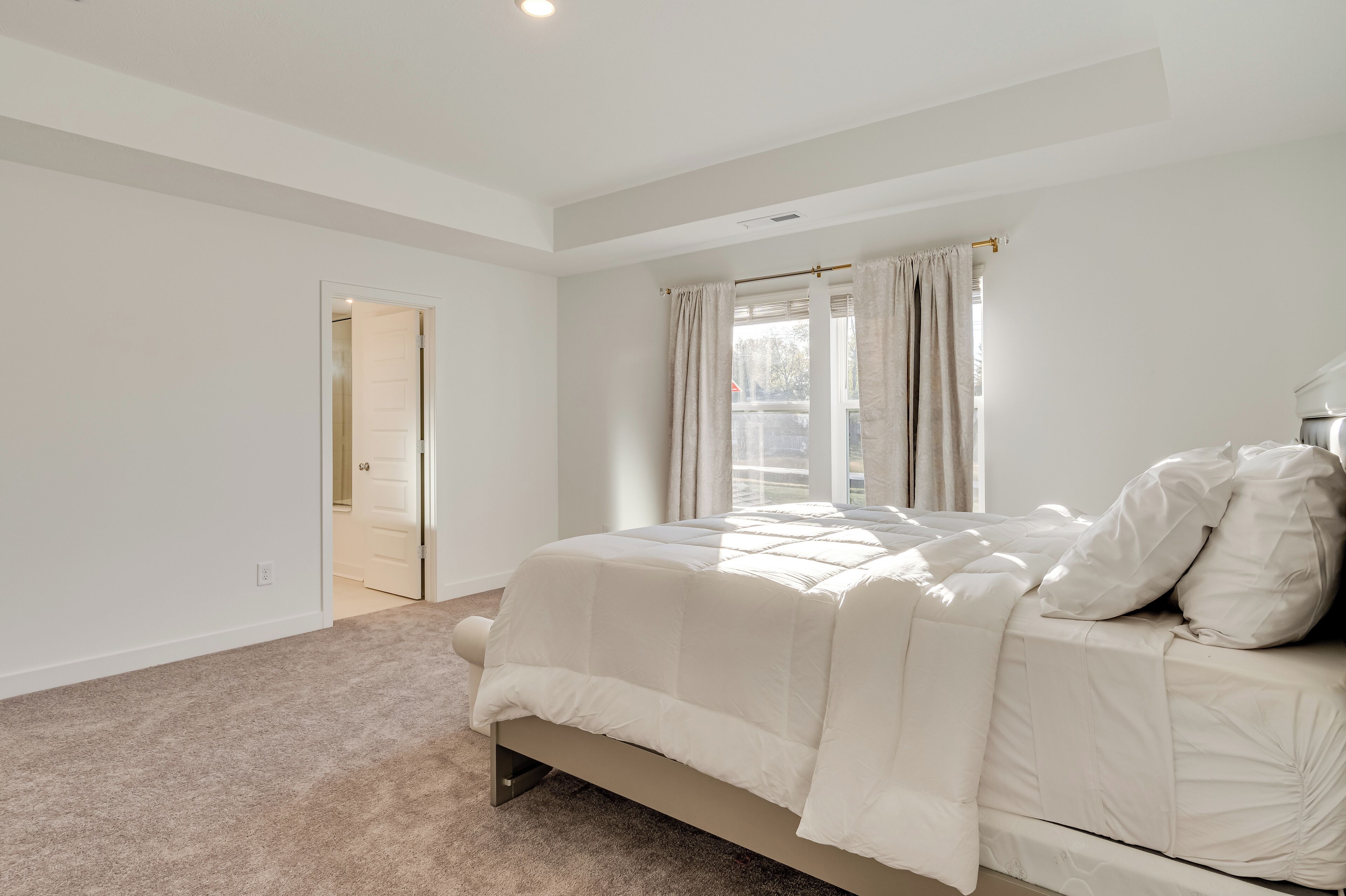 A bedroom with a bed, a window with curtains, and a door leading to another room.